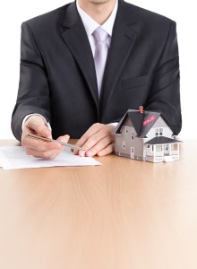 Real estate concept - business-man signs contract behind househo